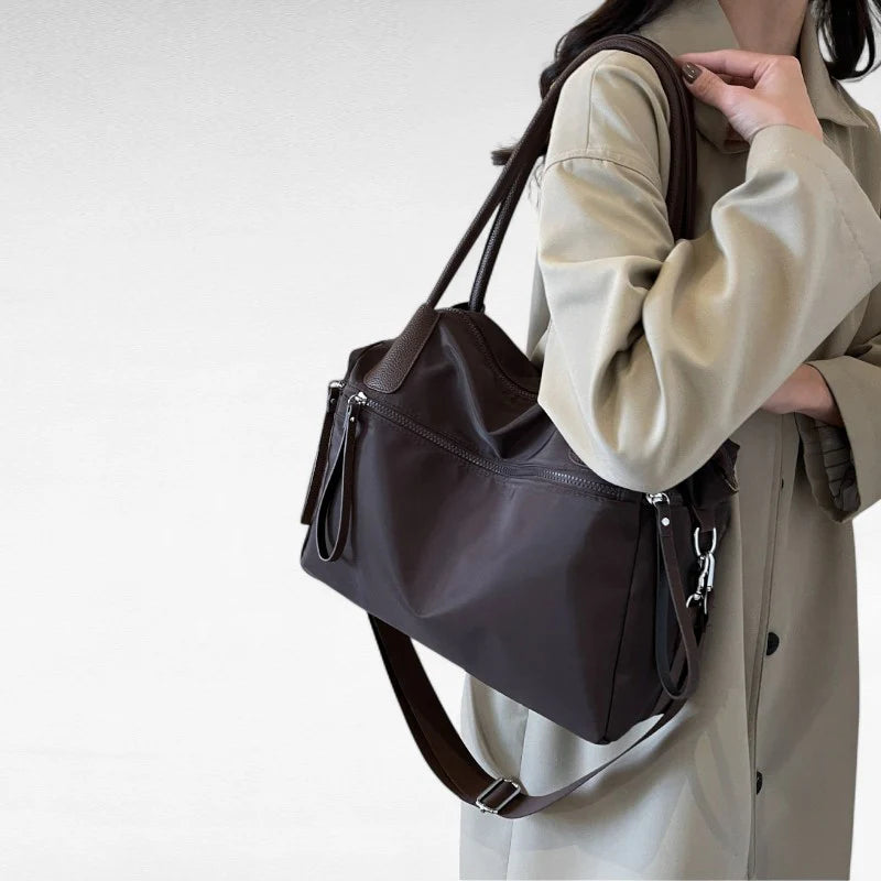 Sac à main NARA café en toile résistante, léger et pratique, avec bandoulière ajustable, offrant grande liberté de mouvement pour vos essentiels du quotidien, porté épaule.